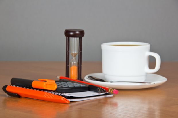 A cup of espresso next to an hourglass-style egg timer and a notepad