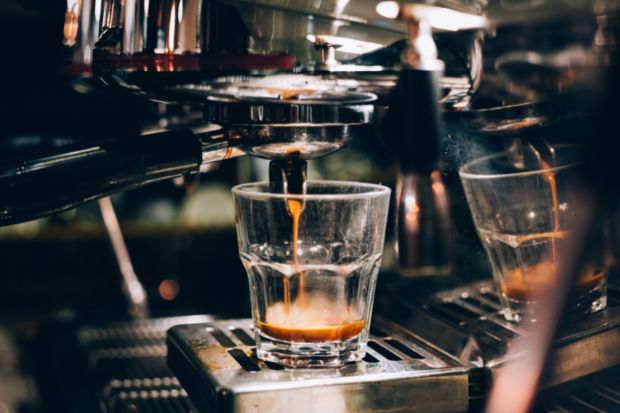 Espresso machine pouring espresso into clear glass as barista begins timing espresso shots