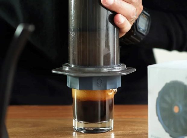 A person presses down on an AeroPress that has the Fellow Prismo attached