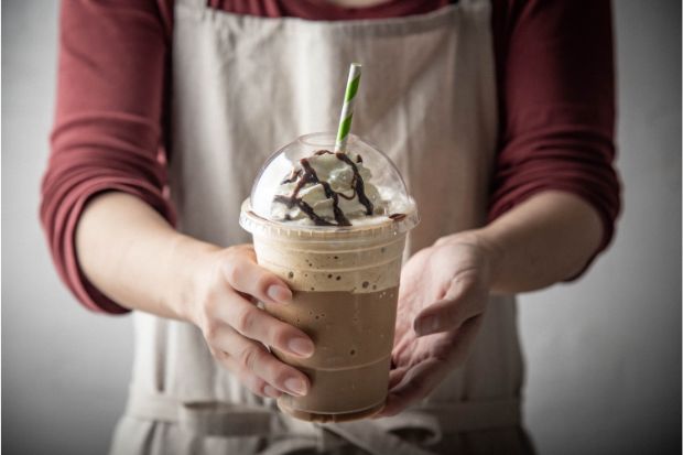 A barista in an apron holds out a Frappuccino