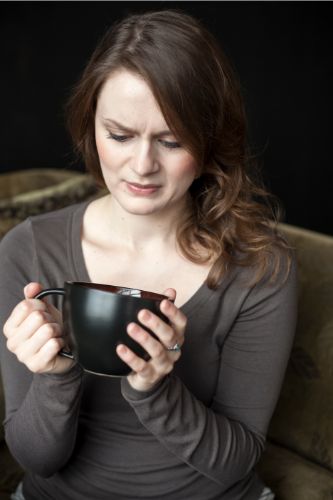 Woman looking disgusted after reheating coffee and taking sip