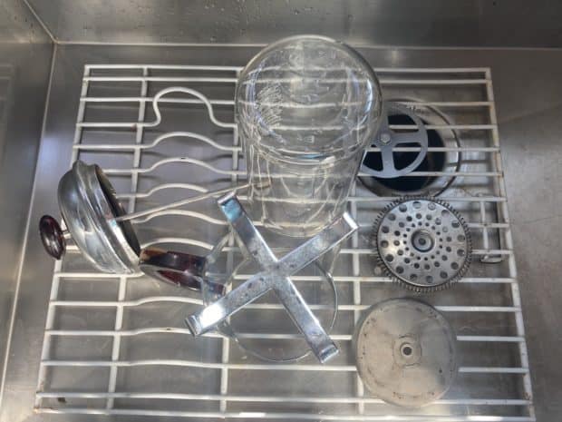 A disassembled French press dries on a rack in the sink after cleaning