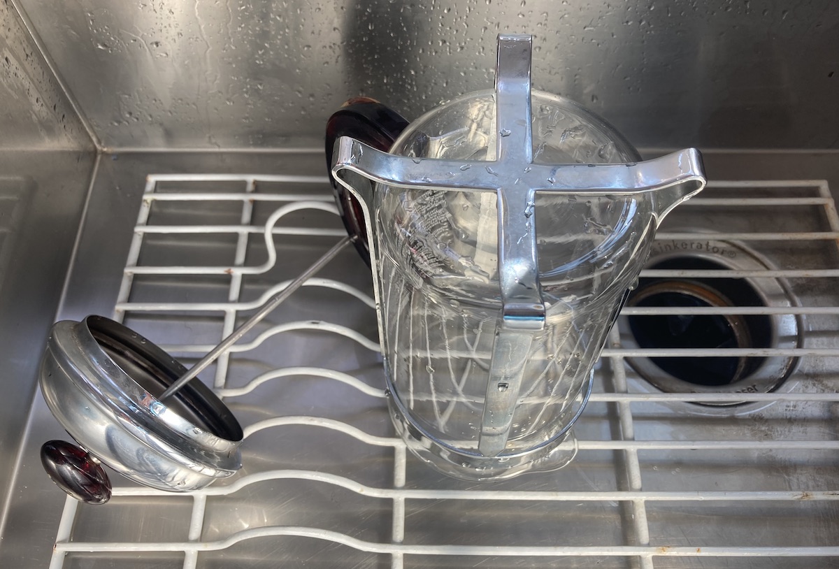 A French press drying upside down on a rack in a sink after cleaning