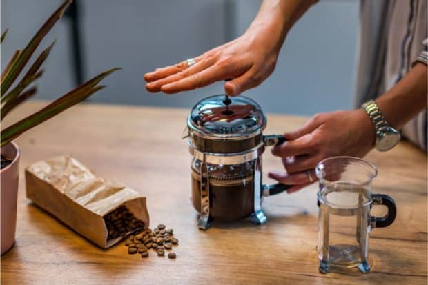 Woman pressing down on French press coffee maker after steeping coffee