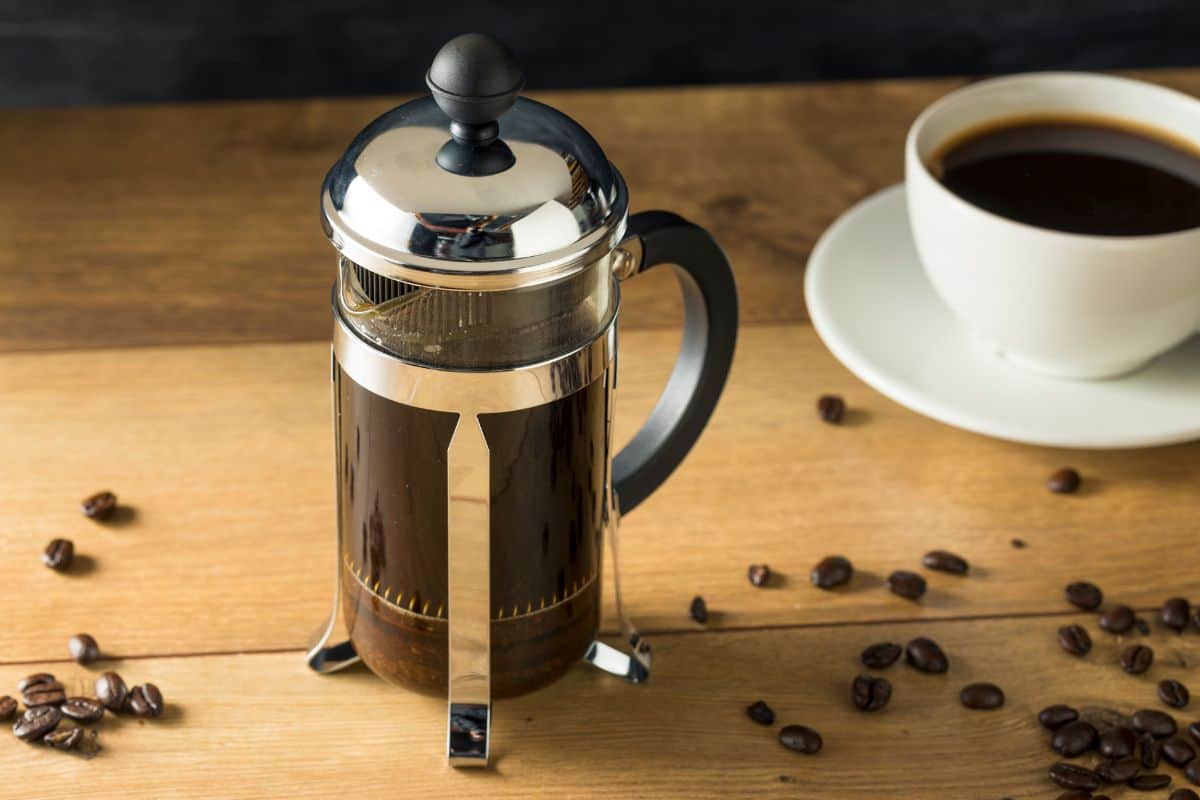 French press steeping next to a cup of coffee