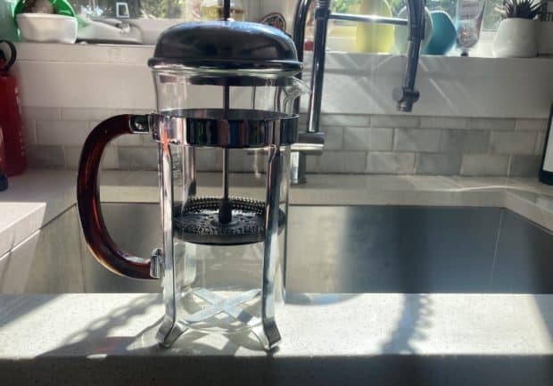 A clean French press gleams in the sun on a kitchen counter