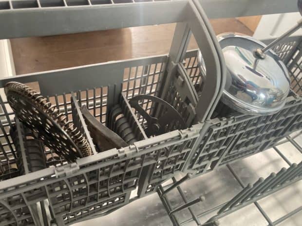 Pieces of a disassembled French press ready for cleaning in the cutlery rack of a dishwasher