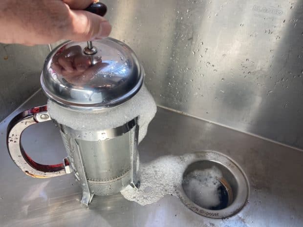 A hand plunges a French press full of soap suds in the sink