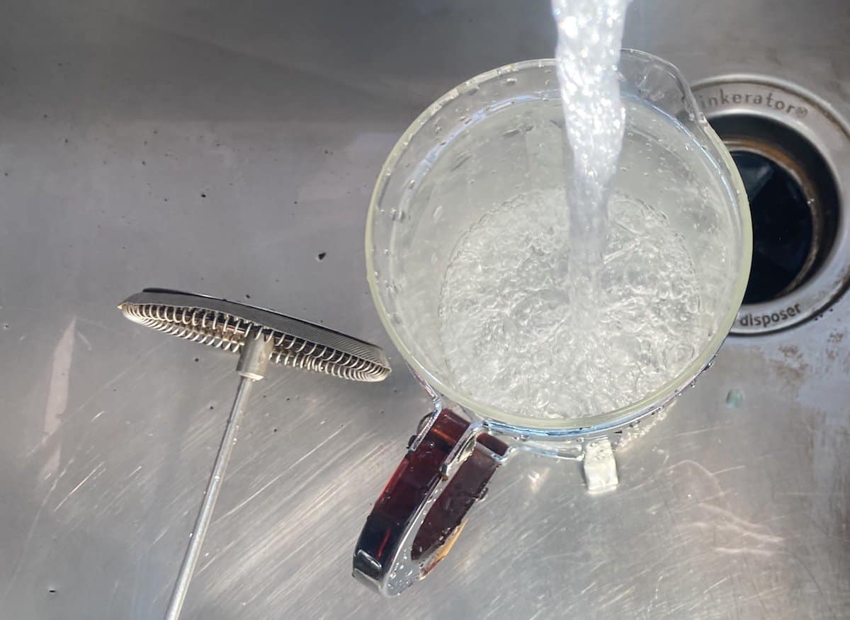 Water from a tap rinsing a French press in a stainless steel sink