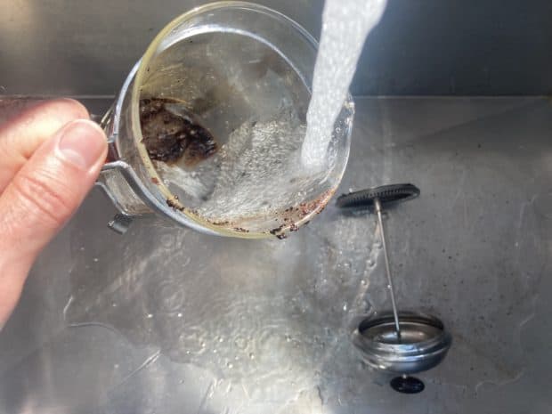 A dirty French press being rinsed in the sink