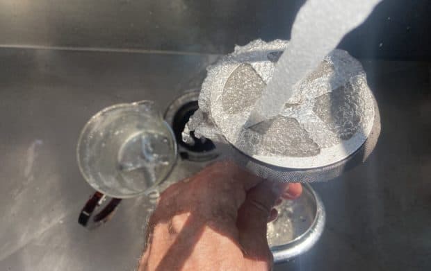 Water pouring from a kitchen sink tap onto the plunger of a French press