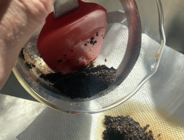 A rubber spatula scoops coffee grounds out of a dirty French press