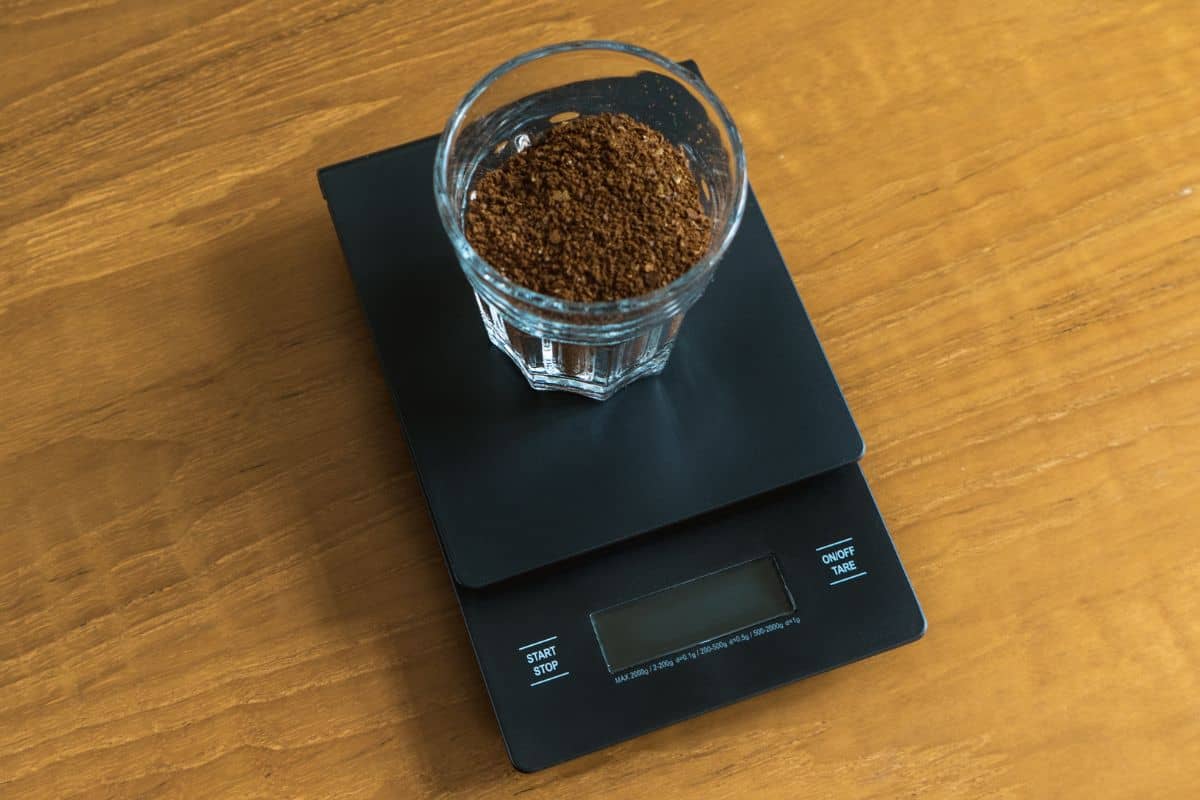 Coarse coffee grounds in a glass being weighed on a scale