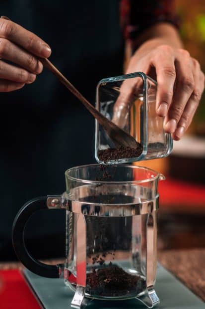 Pouring coffee grounds into French press for the right ratio