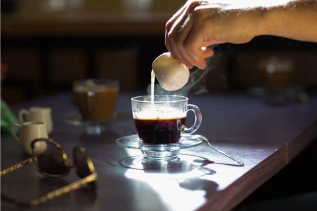 Hand pours heavy whipping cream into an espresso