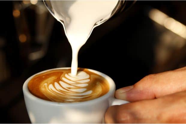 Hands pouring milk into espresso to make a latte