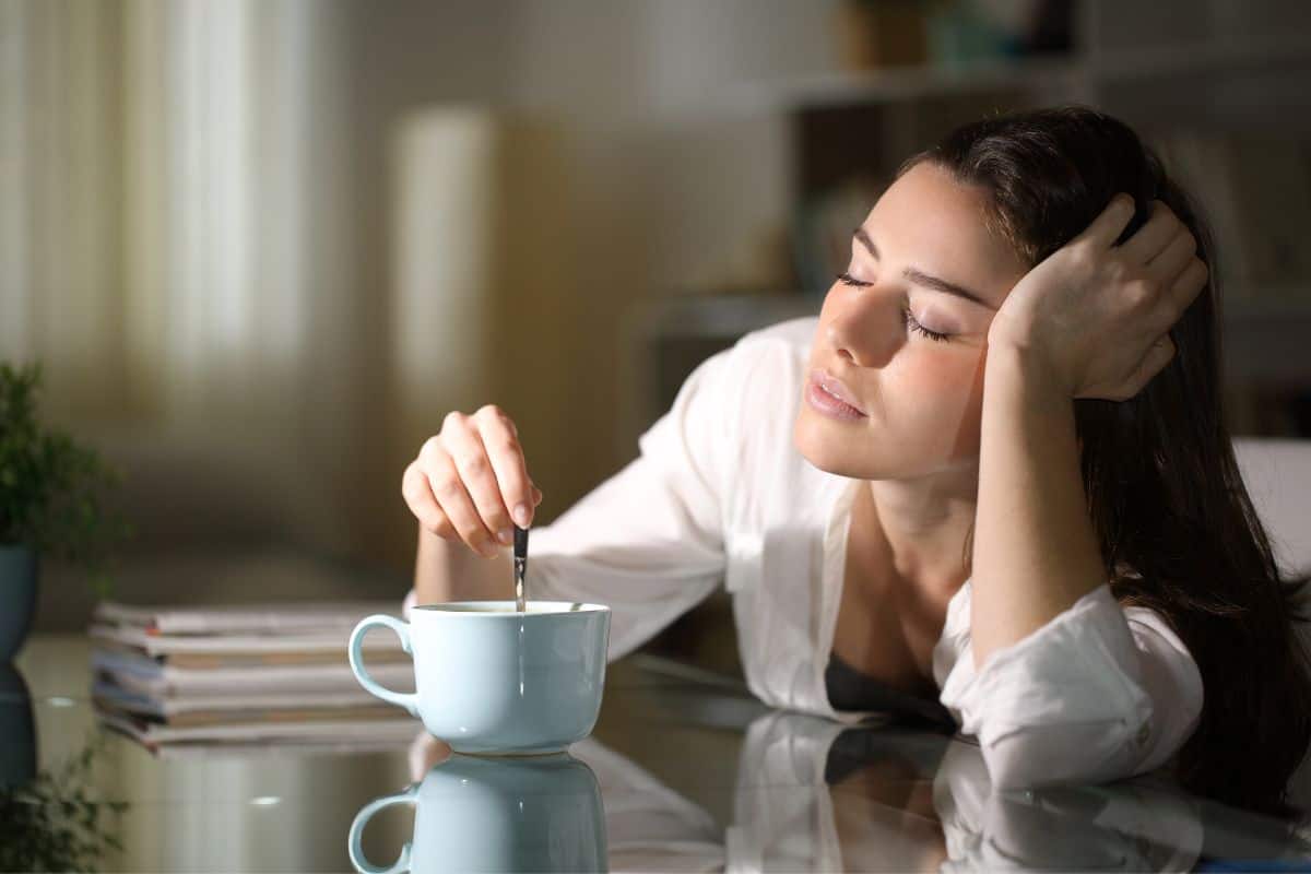 Woman half asleep while stirring cup of coffee