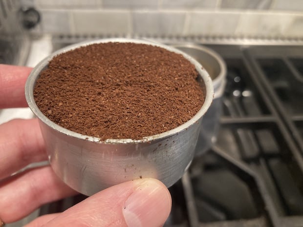 A moka pot filter basket filled to the rim with coffee grounds and levelled off