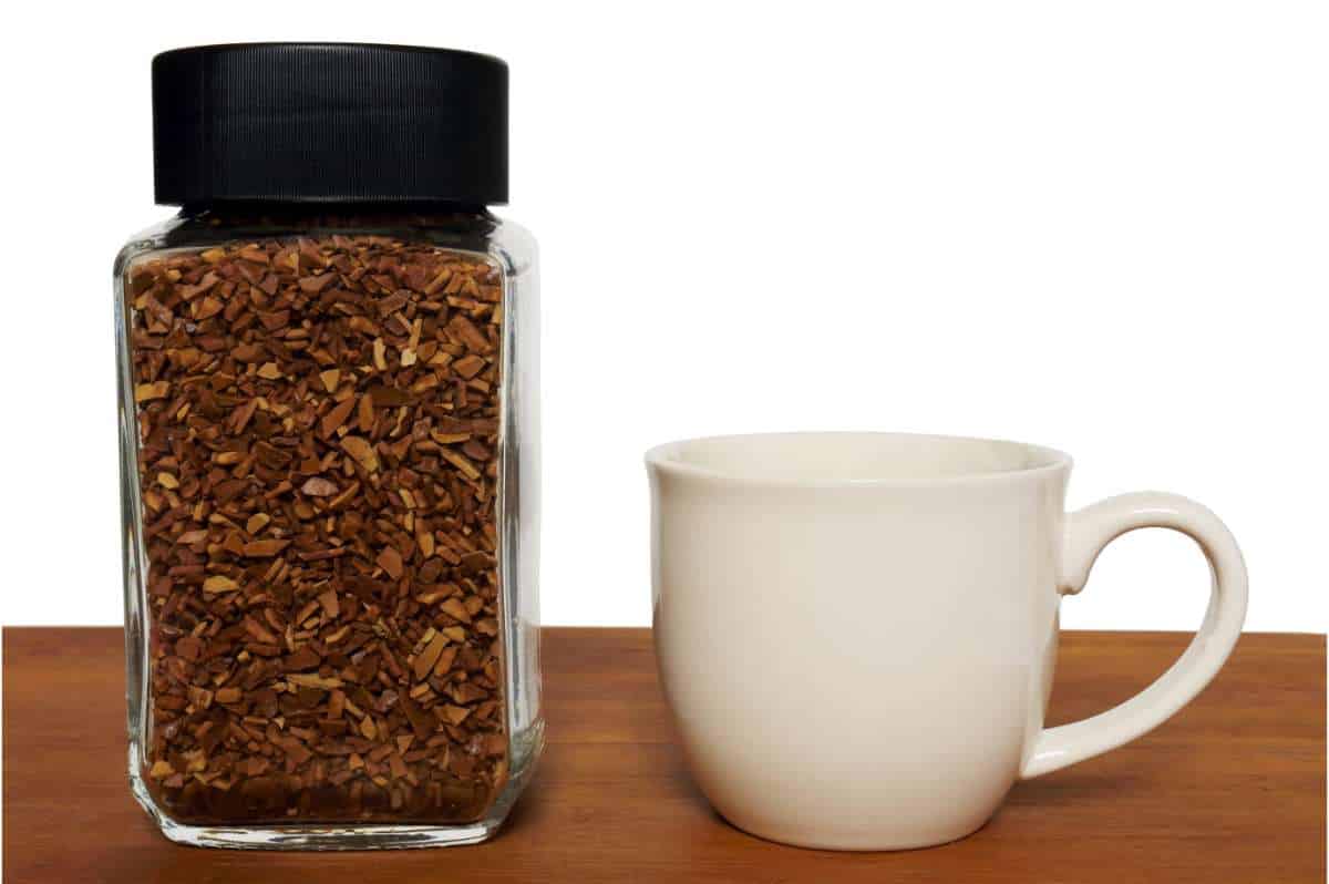 Jar of instant coffee granules next to a white coffee cup