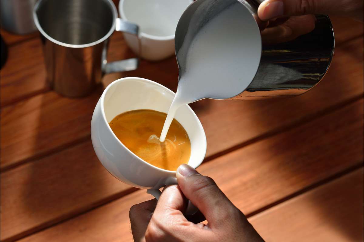 Hands pouring milk from a pitcher into a cappuccino cup