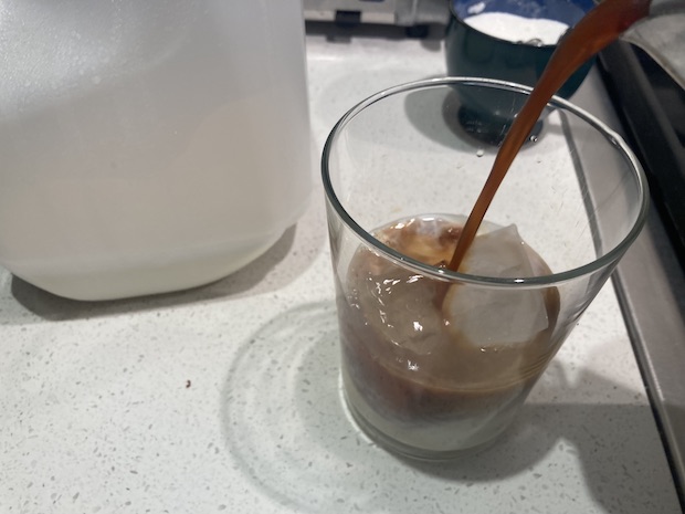 Coffee being poured from a moka pot into a glass of milk and ice