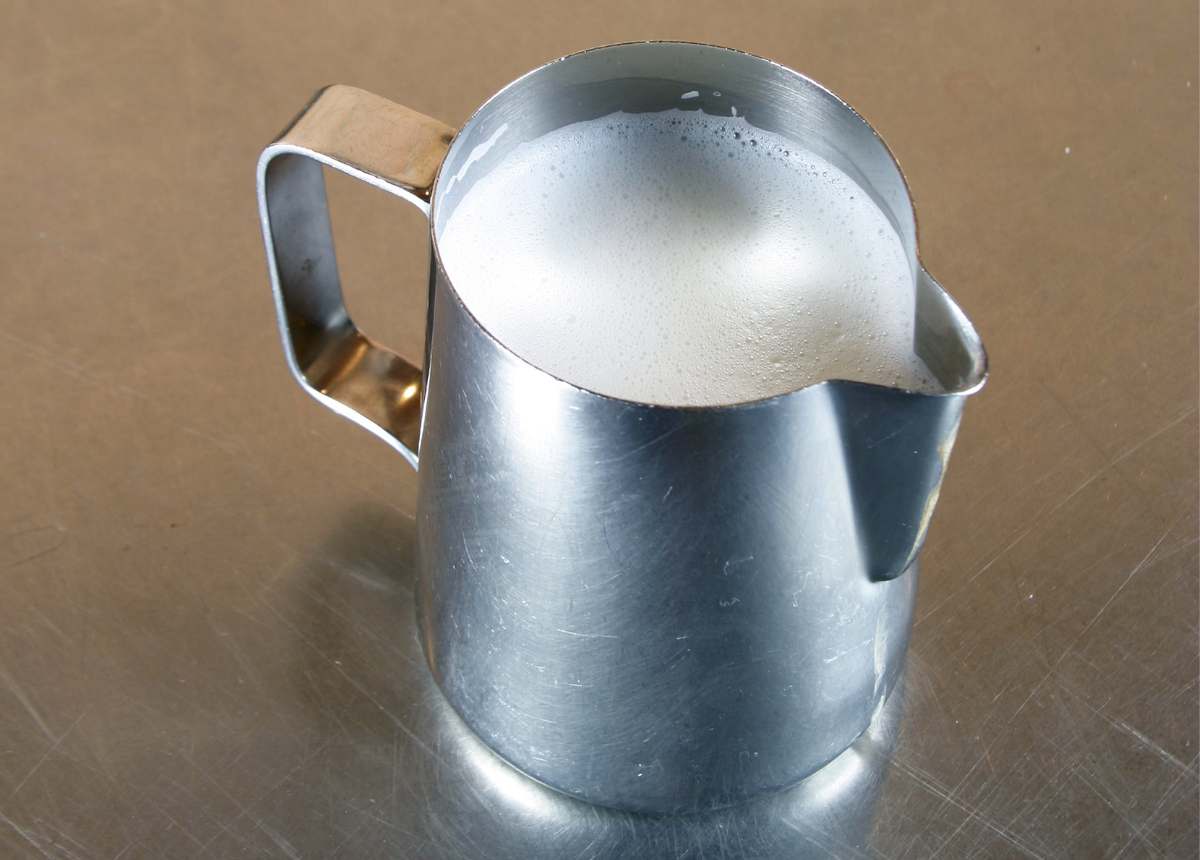 Barista milk pitcher full of frother milk on a counter