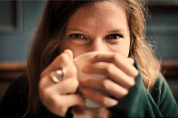 Woman peering over a coffee cup toward the camera as she sips