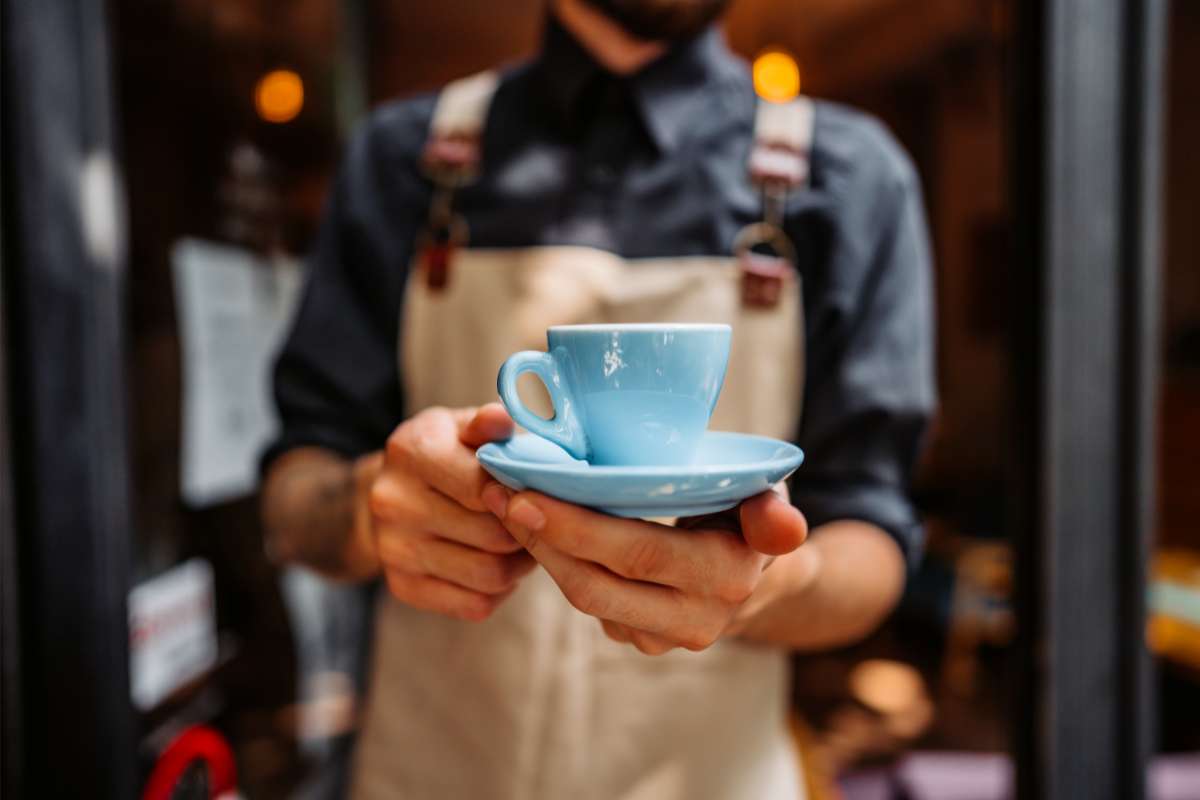 Barista in an apron holding out a light blue coffee cup