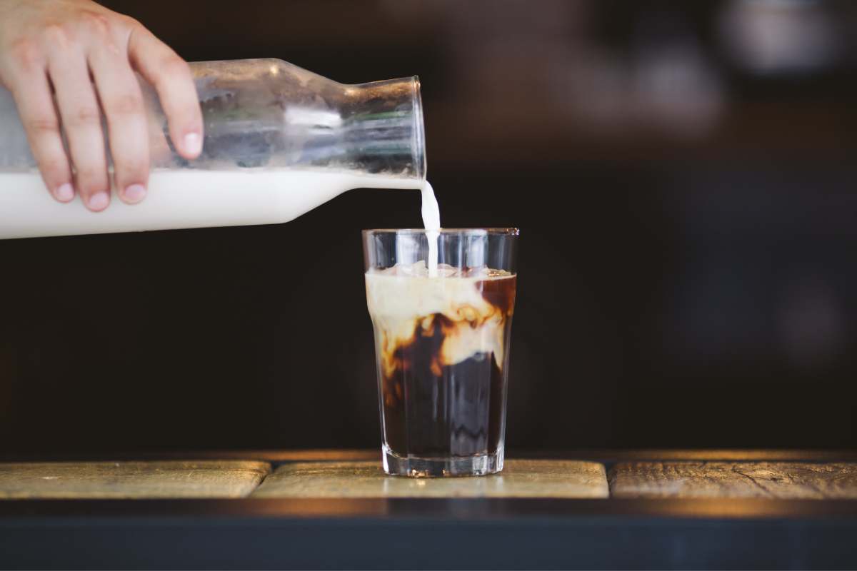 Hand pouring milk into a tall glass of cold brew