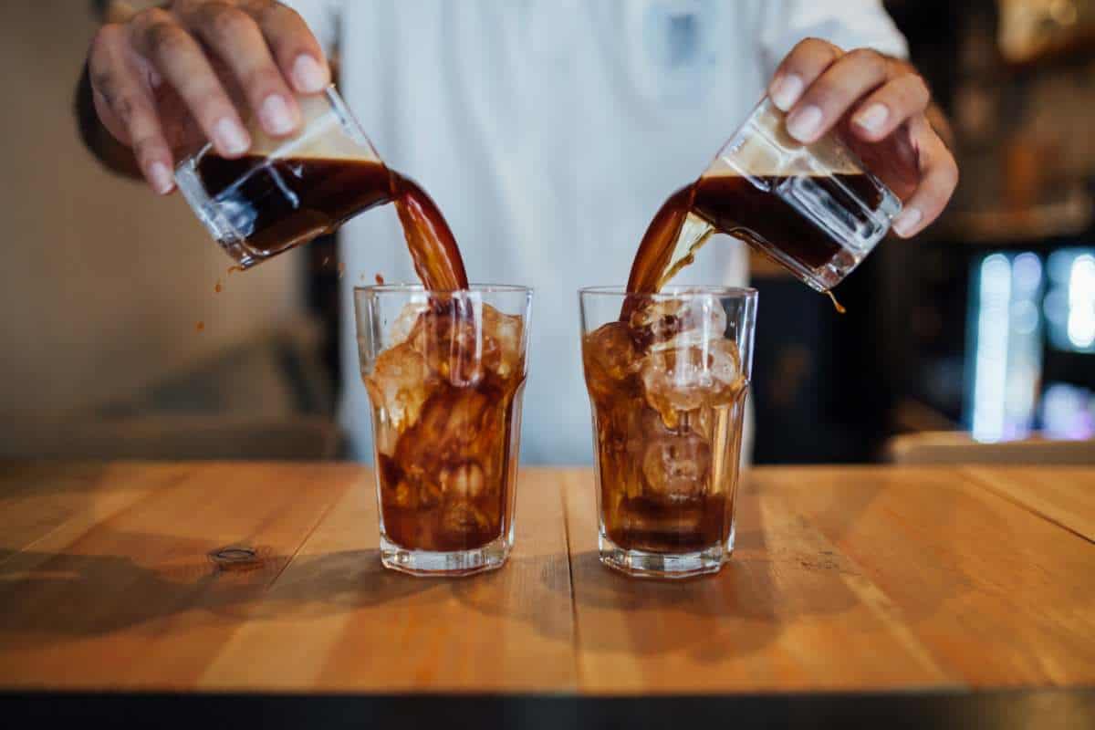 Barista's hands pouring two cold brews over ice at the same time into separate glasses
