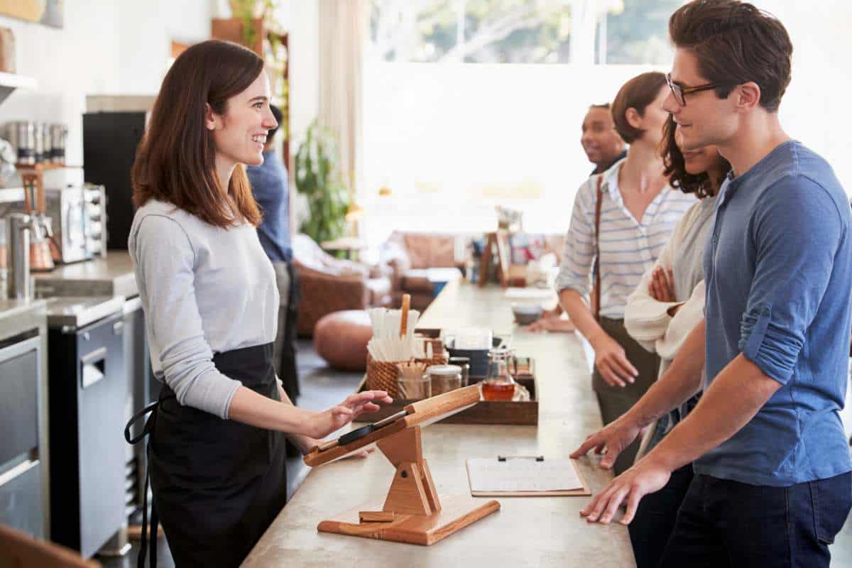 Customers in a good mood chat with barista woman at a coffee shop