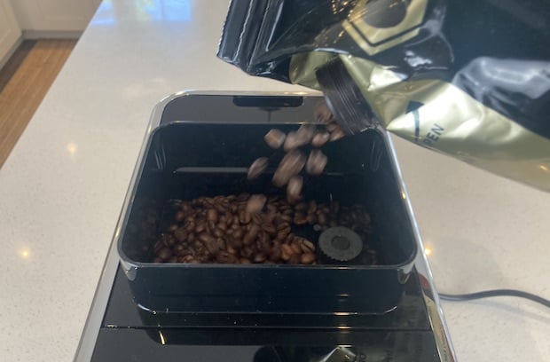 Coffee beans pouring from a bag into the hopper of the Tchibo coffee machine