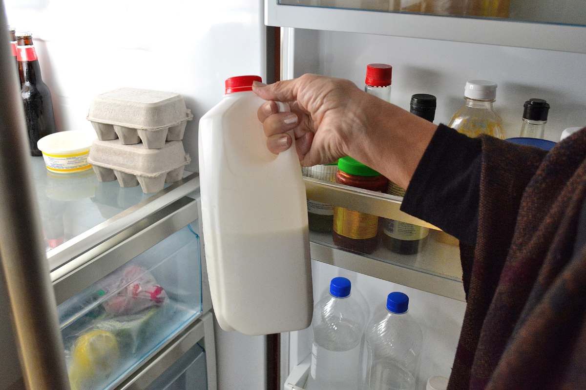 Man's arm removing cold milk jug from refrigerator