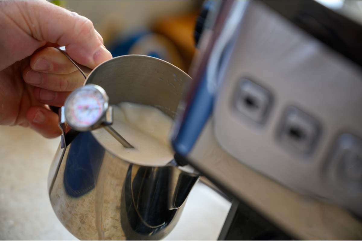 Milk being frothed by an espresso machine with a thermometer in the milk jug
