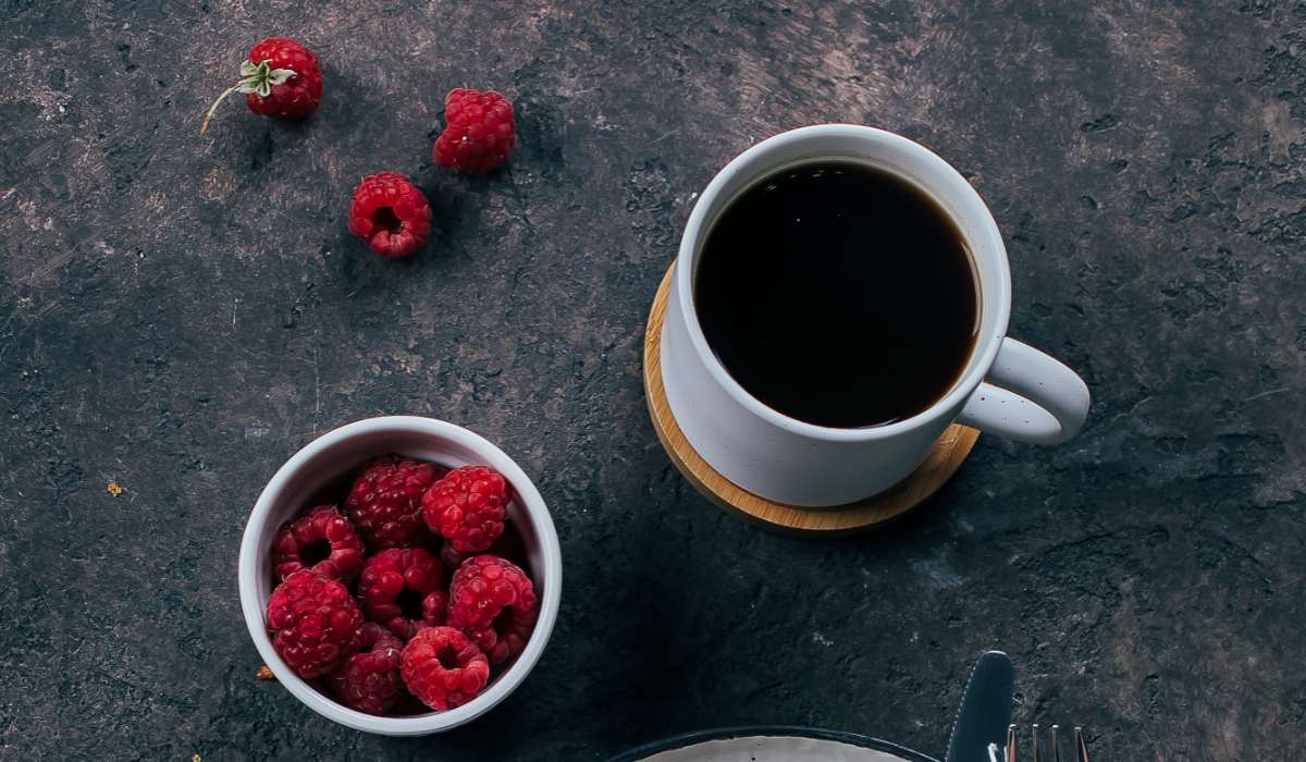 A coffee cup next to a bowl of raspberries