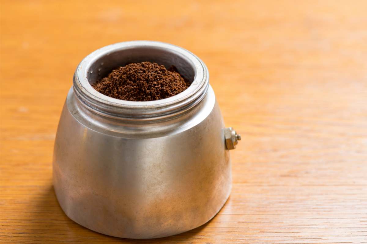 Base of a moka pot with the filter basket inserted and filled with ground coffee