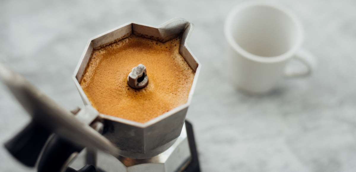 Moka pot full of coffee next to a small espresso cup