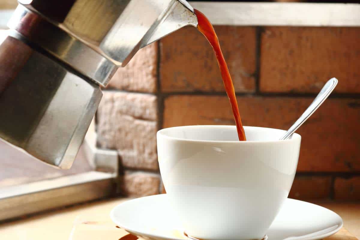 Coffee pouring from a moka pot into a white cup