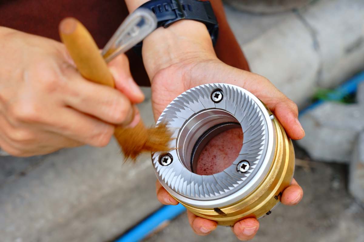 A pair of hands brushes coffee grounds from the burr of a grinder