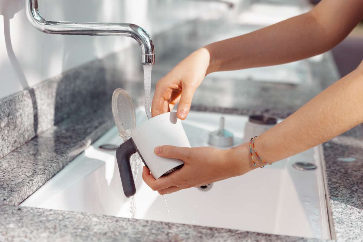 A pair of hands cleaning a moka pot in a sink