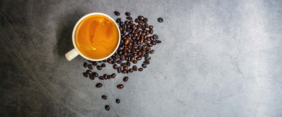 An overhead view of an espresso with nice crema, surrounded by coffee beans