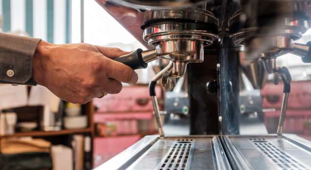 A man's hand locks a portafilter into place on an espresso machine