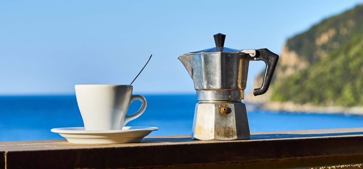 Moka pot and coffee cup on the railing of a balcony by the Mediterranean Sea